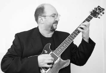 (Picture of Mark Smart playing a guitar in a black jacket and looking REALLY studly.)
